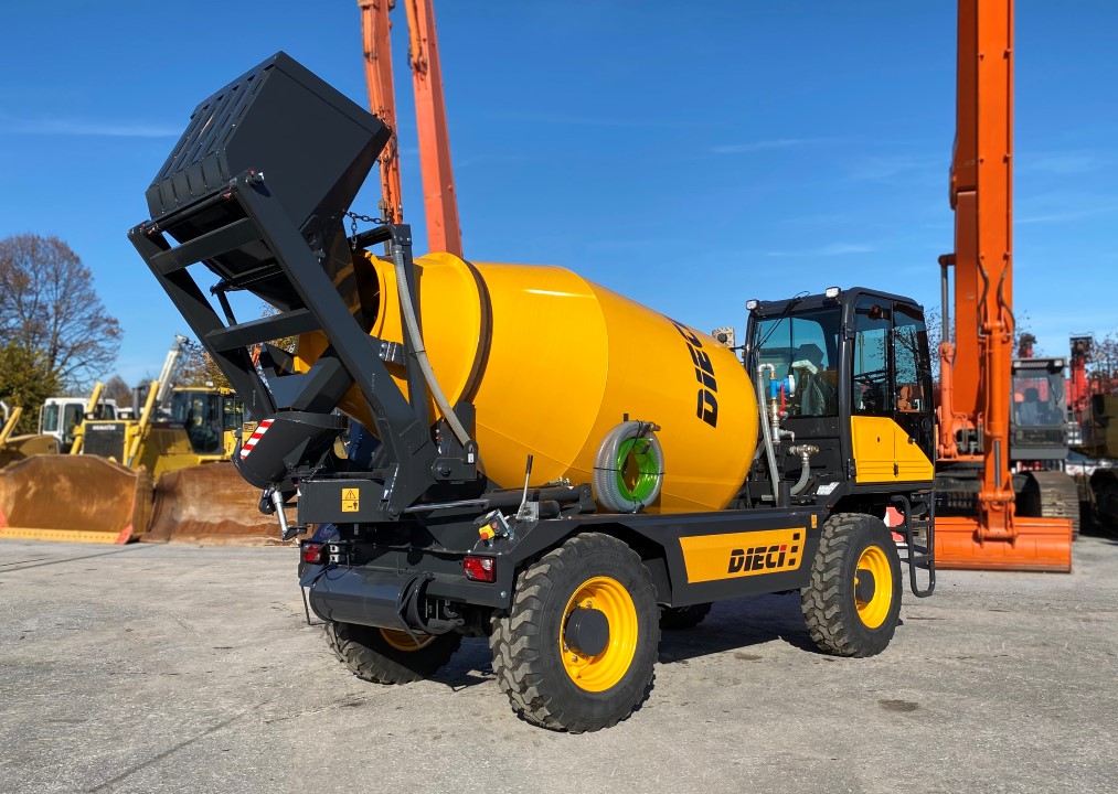 A bright yellow Dieci concrete mixer truck is parked outdoors on a sunny day, surrounded by other construction machinery and equipment. The mixer drum is tilted, and the truck is on a paved surface.